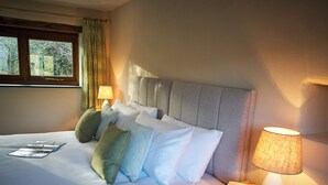 Un lit bien fait, agrémenté de plusieurs oreillers, une table de chevet avec une lampe et une fenêtre avec des rideaux.