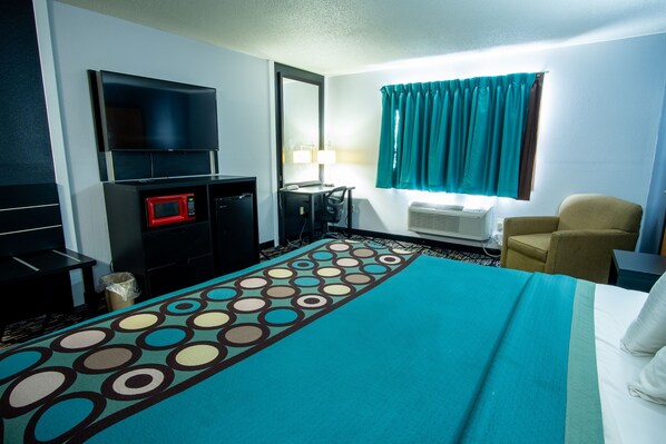Habitación de hotel con cama, escritorio con computadora, microondas, televisión y ventana con cortinas.