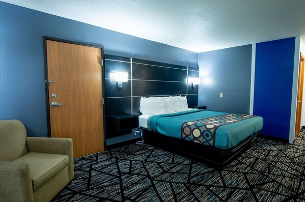 Relax in a stylish room with a large bed, headboard with lighting, and a comfortable armchair.