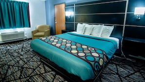 Una habitación de hotel con cama, una silla, un escritorio y una ventana con cortinas.