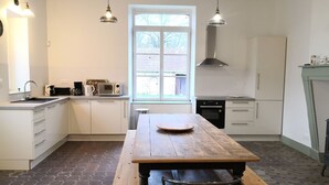 Een keuken met witte kasten, een houten tafel en een raam met uitzicht op een bakstenen gebouw.
