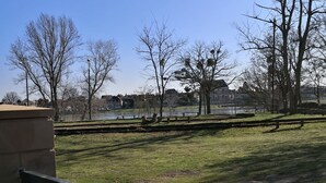 Een park met een gazon, bomen, een bankje en een waterpartij op de achtergrond.