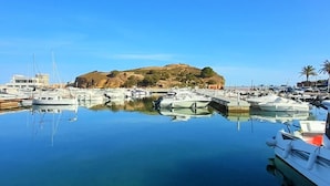 Een jachthaven met aangemeerde boten, een heuvel met ruïnes en helderblauwe lucht.