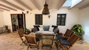 Een terras met een glazen tafel, omringd door houten stoelen, een hanglamp en potplanten.