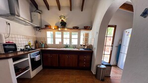 Una cocina con suelo de baldosas, armarios de madera, un fregadero, una estufa y un microondas.