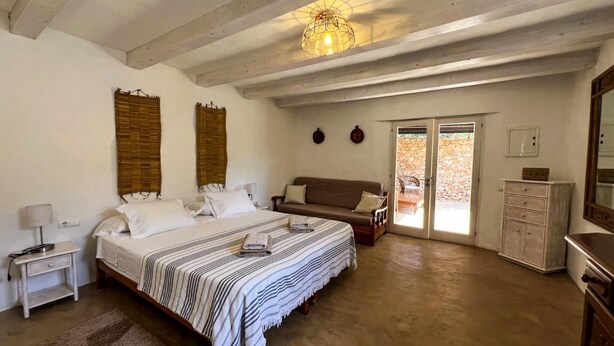 Een slaapkamer met een groot bed, een houten dressoir, een bank en een plafondlamp.