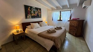 Un dormitorio con cama, mesita de noche, cómoda, un cuadro y una ventana con cortinas.