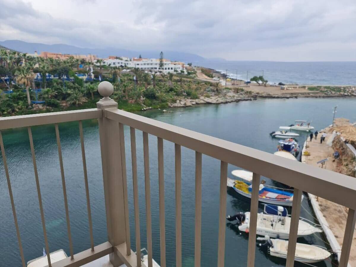 A balcony overlooking a marina with boats, a coastal town in the background, and a clear sky.
