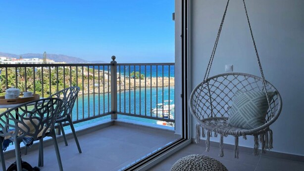 Un balcón con vistas al mar, una silla colgante y una mesa con sillas.