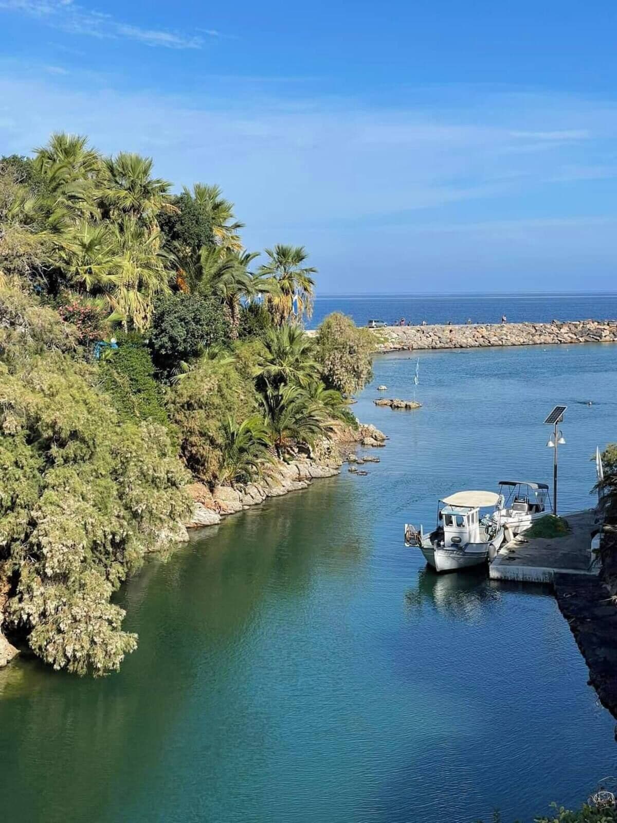 A calm river with boats docked, surrounded by lush greenery and a rocky shoreline.