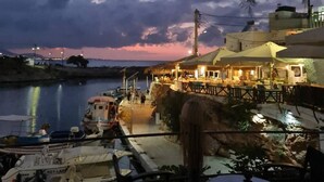 Restaurante frente al mar con terraza al aire libre, con vistas a un cuerpo de agua y al atardecer.