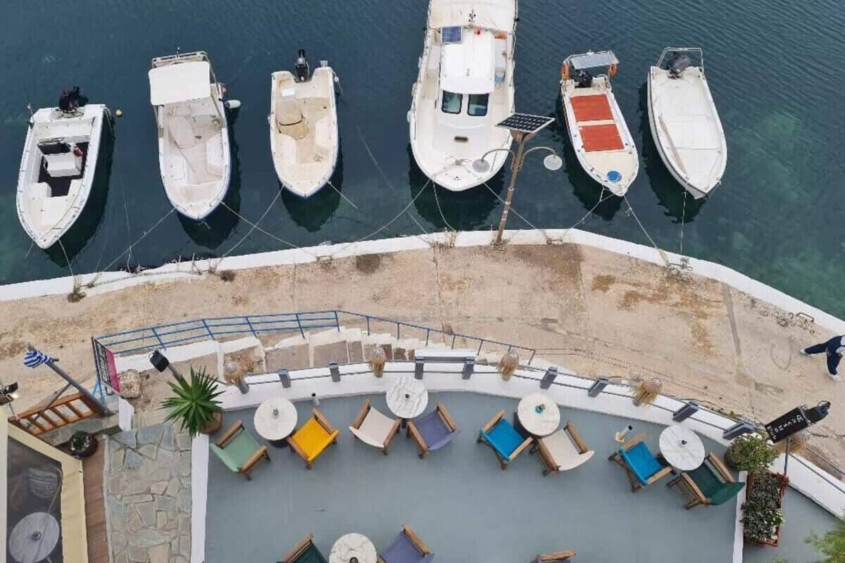 A marina with several boats docked, a sandy beach, and a seating area with tables and chairs.