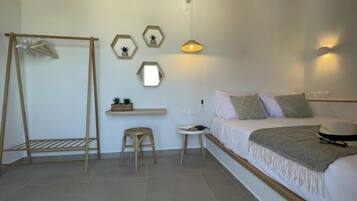 Un dormitorio con cama, una silla de madera, un taburete pequeño, una estantería con plantas y una lámpara de pared.