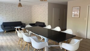 A modern dining area with a long table, white chairs, a dark sofa, and patterned wallpaper. - Villa with sea access and spa (Saint-Vincent-sur-Jard)
