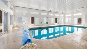Ein großes Hallenbad mit klarem, blauem Wasser, umgeben von weißen Wänden und großen Fenstern.