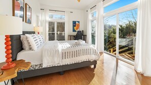 Ein Schlafzimmer mit einem Bett, einem Schreibtisch, einem Stuhl, einem Deckenventilator und großen Fenstern.