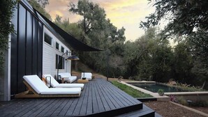Eine Terrasse mit Liegestühlen, einem Pool und einem Haus mit großen Fenstern.
