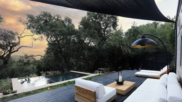 Eine Terrasse mit Sitzgelegenheiten im Freien, einem Pool und Blick auf Bäume.