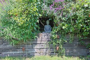 A statue in a garden setting with a wooden wall and various plants.