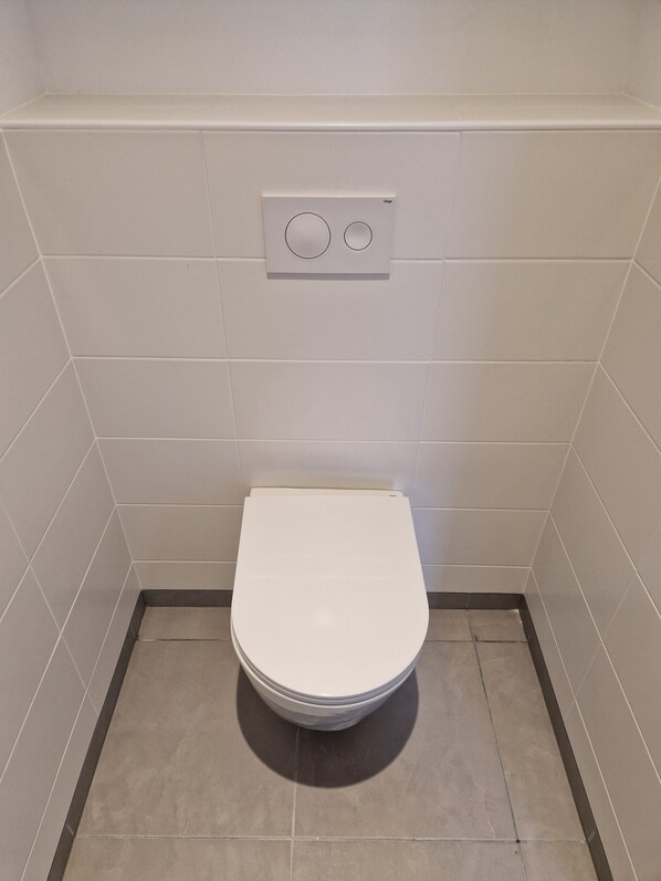 A small, white toilet in a corner with a control panel above it.