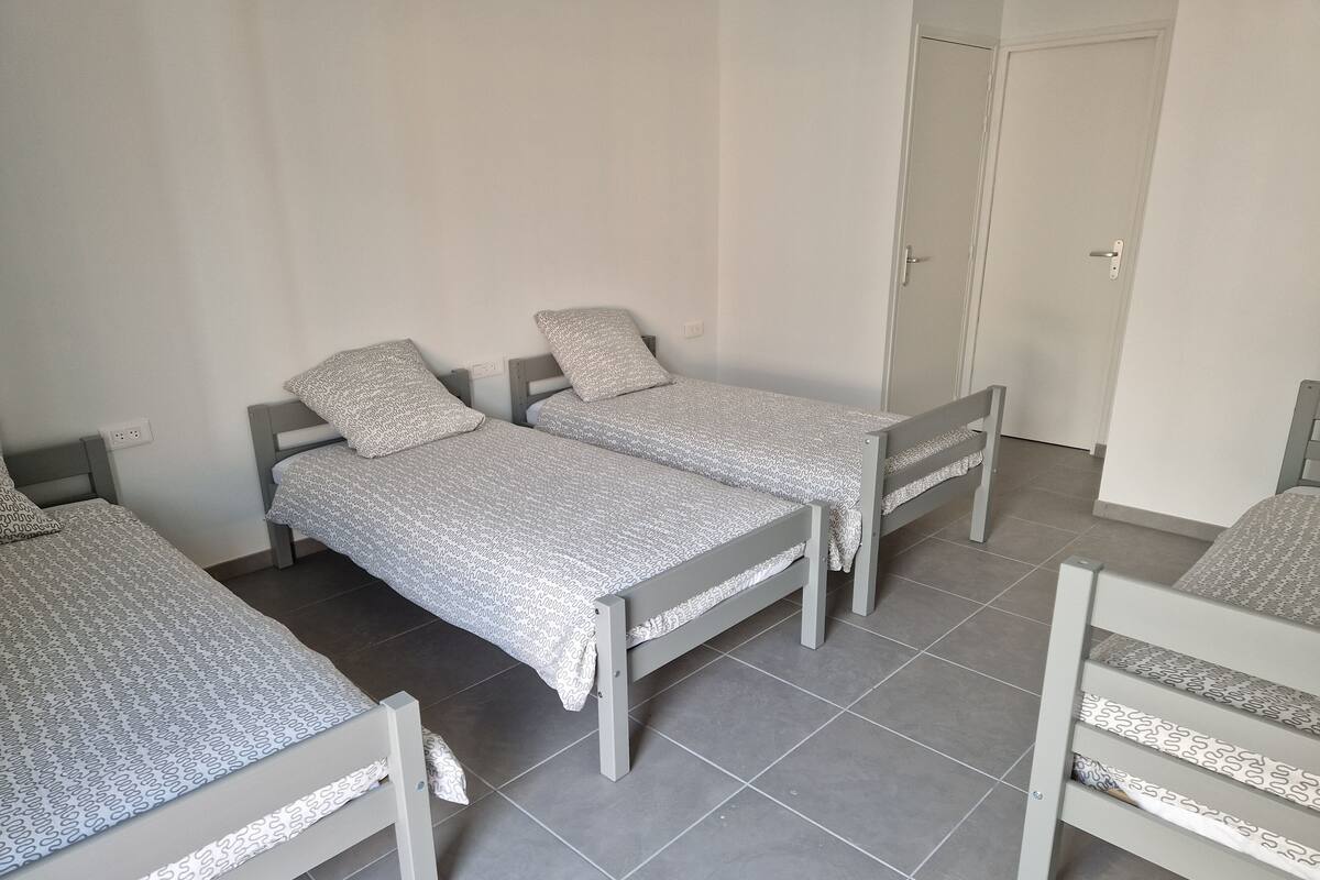 Une chambre avec trois lits simples, chacun doté d’un cadre gris et de draps à motifs.