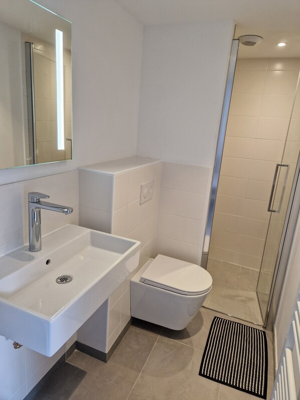 Un baño moderno con lavamanos blanco, inodoro y zona de ducha.