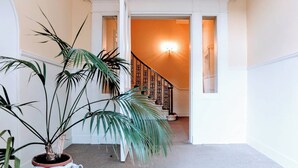 Ein Flur mit einer Treppe zu einer oberen Etage, einem Blumentopf und einer weißen Kanne auf dem Boden.