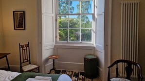 Ein Zimmer mit großem Fenster, einem Bett, einem Sessel, einem kleinen Tisch und einer Heizung.