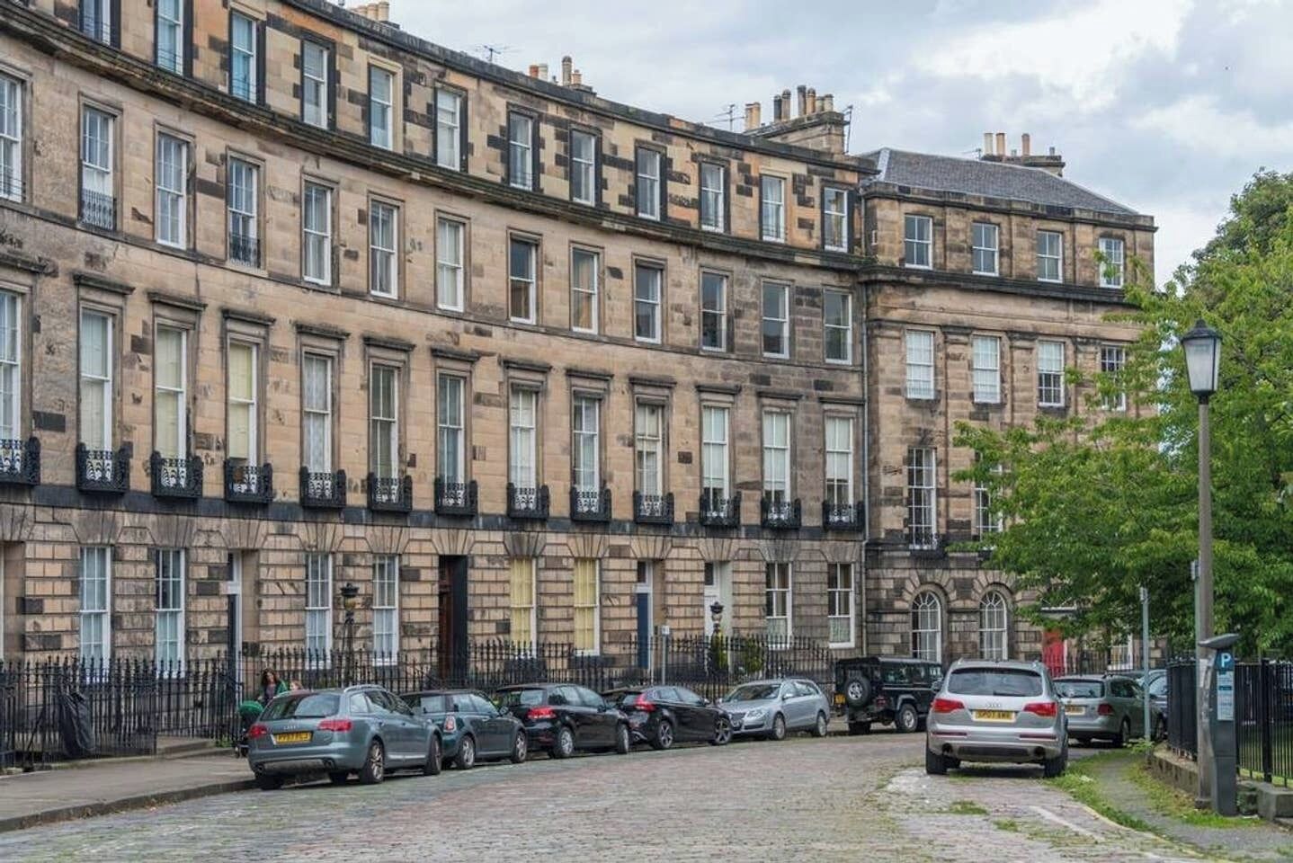 Una hilera de casas escalonadas con una calle adoquinada y coches estacionados.