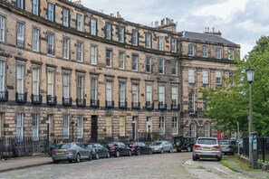 A row of terraced houses with a cobblestone street and parked cars. - JOIVY Gorgeous Georgian Flat (Edinburgh)