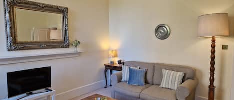Sala de estar com televisão, sofá, mesa de centro e objetos decorativos.