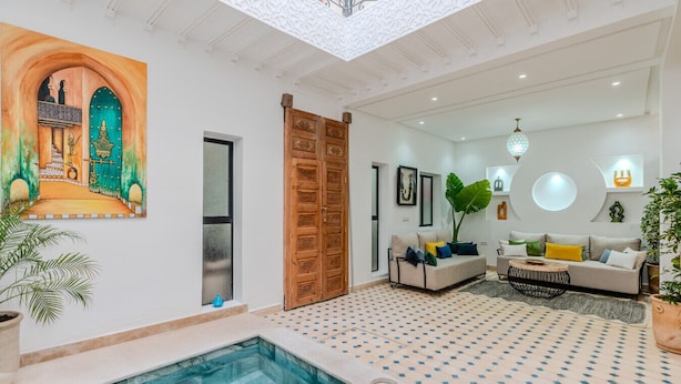 A modern living room with a pool, a large wooden door, and a colorful mural on the wall. - Riad Dar Amarena - Exclusif - BreakFast (Marrakech)