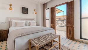 A bedroom with a bed, a bench, a door leading to a balcony, and a wall-mounted light fixture. - Riad Dar Amarena - Exclusif - BreakFast (Marrakech)