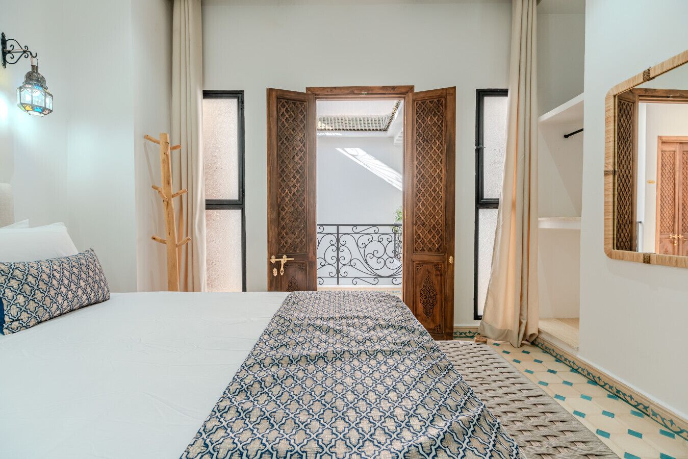 A bedroom with a bed, a wooden door, a balcony, and a hanging light fixture.