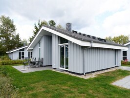 A modern two-story house with a sloped roof, large windows, and a patio area with outdoor furniture.