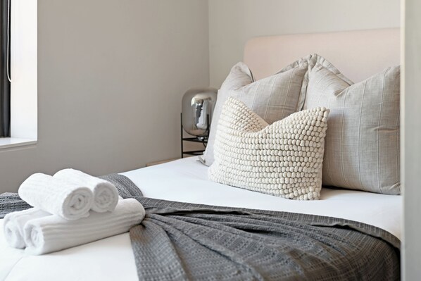 A neatly made bed with rolled white towels, a gray throw blanket, and a textured white pillow.
