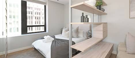 A modern bedroom with a bed, a built-in bench, a window, and a wall-mounted shelf with decorative items.