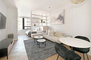A modern living room with a sofa, two round tables, and a TV. - 1-Bed Hideaway | High-Rise with City Views (Cape Town)