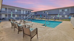 A hotel with a swimming pool, outdoor seating, and a staircase leading to the upper floors.