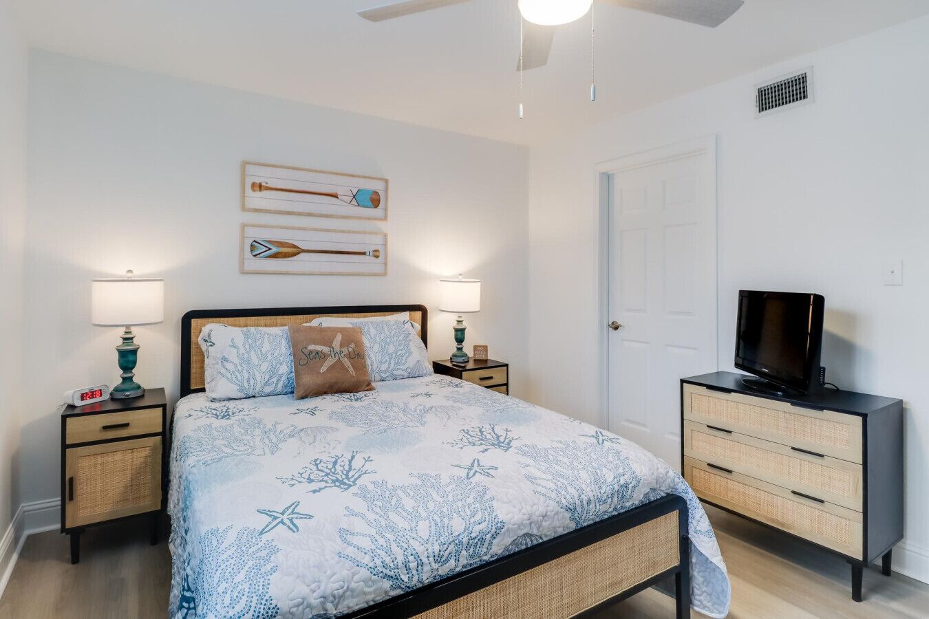 A bedroom with a bed, two bedside tables, a television on a dresser, and a ceiling fan.