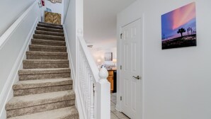 A staircase leading to a kitchen area with a white door and a painting of a sunset.