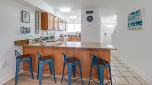 A modern kitchen with a central island, bar stools, wooden cabinets, and a clock on the wall.