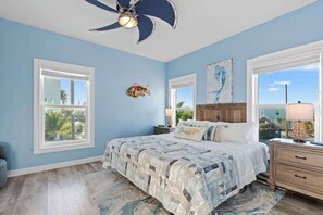A bedroom with a bed, a ceiling fan, a nightstand, a lamp, and a view of the outside.