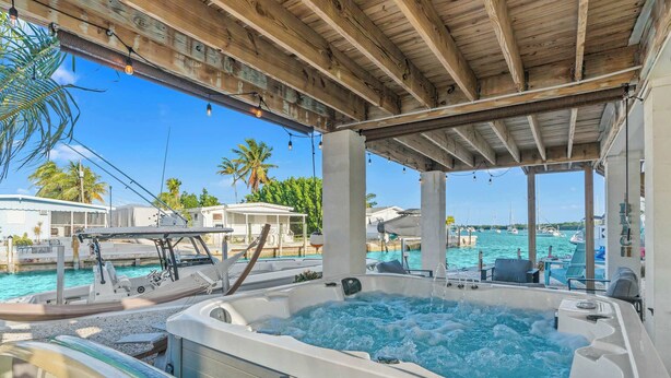A covered outdoor area with a hot tub, lounge chairs, and a view of the marina. - Mermaid Manor ~ Waterfront Haven w/ Hot Tub & Dock (Marathon)
