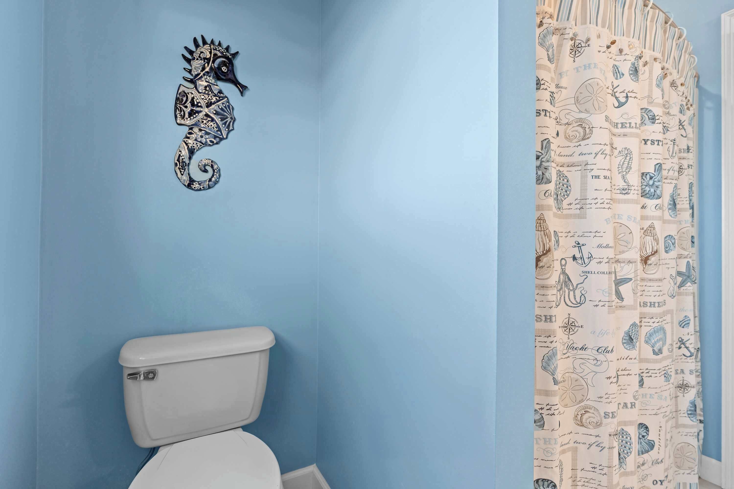Une salle de bain avec un mur bleu, des toilettes blanches et un rideau de douche orné de motifs marins.