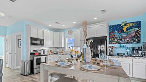 A modern kitchen with white cabinets, a stainless steel range, and a dining area with a wooden table set for a meal. - Mermaid Manor ~ Waterfront Haven w/ Hot Tub & Dock (Marathon)