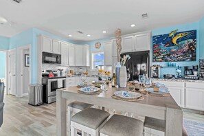 A modern kitchen with white cabinets, a stainless steel range, and a dining area with a wooden table set for a meal. - Mermaid Manor ~ Waterfront Haven w/ Hot Tub & Dock (Marathon)