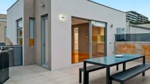 A modern building with a flat roof, a glass door entrance, and a patio area with a table and benches. - Entire Studio With Balcony (Maribyrnong)