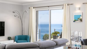Una sala de estar moderna con un sofá, un sillón color turquesa y vistas al mar a través de amplias ventanas.