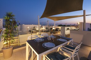 An outdoor dining area with a table set for two, surrounded by chairs, under a large shade structure. - Casa Milhafre - Apartment overlooking Benagil Beac (Benagil)